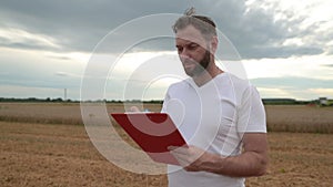 A farmer with a tablet for taking notes stands in a field next to combines working