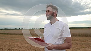 A farmer with a tablet for taking notes stands in a field next to combines working