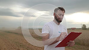 A farmer with a tablet for taking notes stands in a field next to combines working