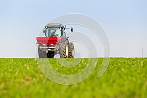 Farmer in tractor fertilizing wheat field at spring with npk