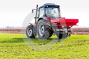 Farmer in tractor fertilizing wheat field at spring with npk