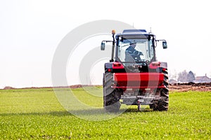 Farmer in tractor fertilizing wheat field at spring with npk