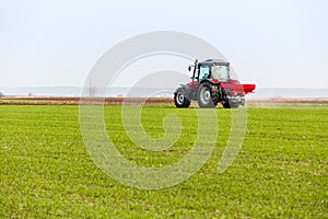 Farmer in tractor fertilizing wheat field at spring with npk