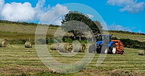 Farmer in tractor making hay bales in field with blue skys , Lozere France