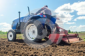 Farmer on a tractor with a milling machine processes loosens soil in the farm field. Preparation for new crop planting. Grind