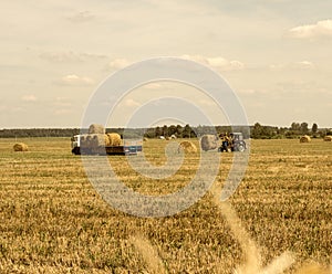 Farmer on a tractor picks haystack and loads bale of hay into the trailer, agriculture