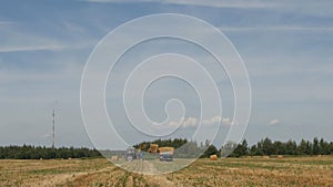 Farmer on a tractor picks haystack and loads bale of hay into the trailer, agriculture