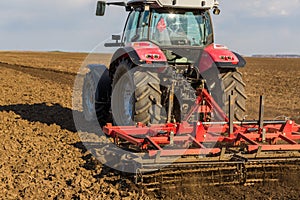 Farmer in tractor preparing land with seedbed cultivator.