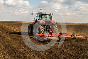 Farmer in tractor preparing land with seedbed cultivator.