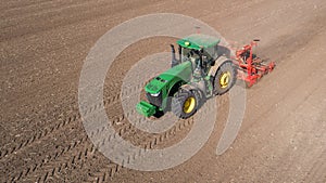 Farmer with tractor with seeder, sowing seeding crops at agricultural field. Aerial view.
