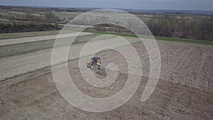 A farmer on a tractor with a seeder sows grain in plowed land in a private field in the village area. Mechanization of spring fiel