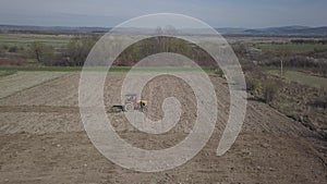 A farmer on a tractor with a seeder sows grain in plowed land in a private field in the village area. Mechanization of spring fiel