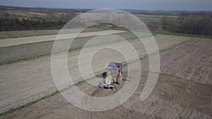 A farmer on a tractor with a seeder sows grain in plowed land in a private field in the village area. Mechanization of spring fiel