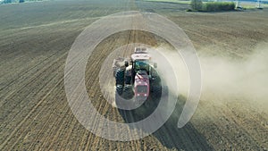 Farmer on tractor with seeding machinery driving over field sows seeds or grain of wheat or corn. Agricultural