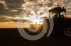 Farmer with tractor seeding - sowing crops at agricultural field in spring