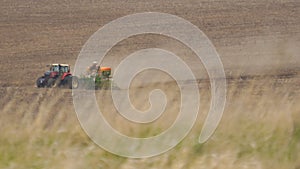A farmer on a tractor sows plowed field with seeds