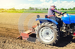 A farmer on a tractor works the field with a shredder in preparation for planting a new crop. Loosens, grind and mix soil.