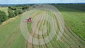 The farmer turns the grass with a hay rake attached to the tractor. Shot from a height.