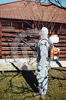 farmer using machine, mistblower for pesticides and insecticide spraying and wearing protective clothing