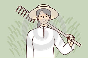 Farmer woman holding rake on shoulder after completing soil preparation for planting crops