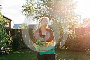 Farmer woman holding wooden box full of fresh raw vegetables. Basket with vegetable cabbage, carrots, cucumbers, radish