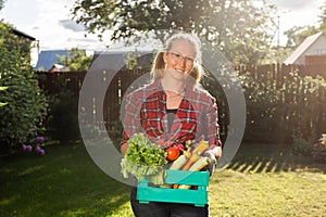 Farmer woman holding wooden box full of fresh raw vegetables. Basket with vegetable cabbage, carrots, cucumbers, radish