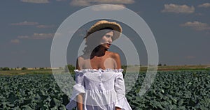 Farmer woman in white dress  and hat stands in a field