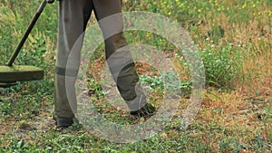 A farmer worker in a work uniform mows the grass with a gasoline trimmer on the lawn in the summer. Grass mowing