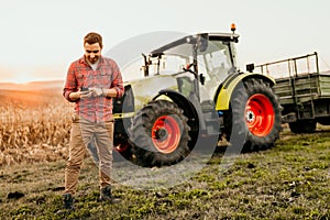 farmer working on field using smartphone in modern agriculture - tractor background