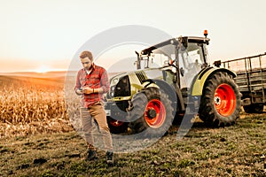 Farmer working on field using smartphone in modern agriculture - tractor background