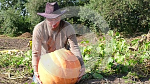 Farmer young man in work clothes and hat on his head holding a pumpkin in his hands