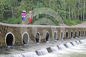 Farmers cross the bridge over the small river to go to the rice fields