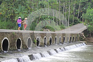 Farmers cross the bridge over the small river to go to the rice fields