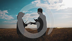 Farmers handshake over the wheat crop in harvest time. Team farmers stand in a wheat field with tablet. Partnership