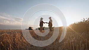 Farmers handshake over the wheat crop in harvest time. Team farmers stand in a wheat field with tablet at sunset