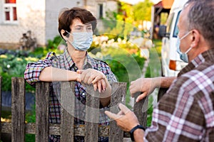 Farmers in protective masks talk while standing at the fence on border of plantation