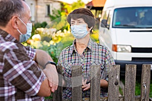 Farmers in protective masks talk while standing at the fence on border of plantation