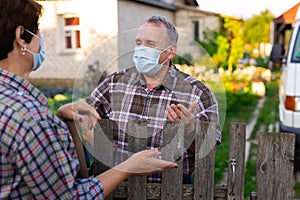 Farmers in protective masks talk while standing at the fence on border of plantation