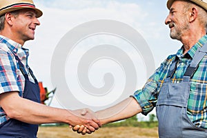 Farmers shaking hands against harvester in field