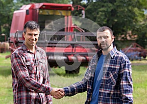 Farmers shaking hands in front of combine harvester