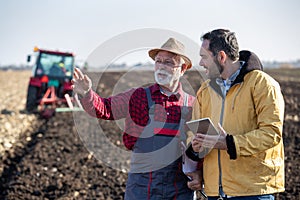 Farmers talking in field in front of tractor in autumn