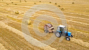 Farmers tractor on wheat field after harvesting makes hay bales. Aerial view on agriculture field with tractor. Harvest time