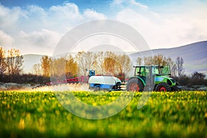 Farming tractor plowing and spraying on the green field photo