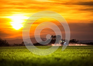 Farming tractor plowing and spraying at sunset