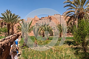 Farmland in front of the scenic berber village Tamenougalt in the Draa valley, a tourist being led by a berber to the village