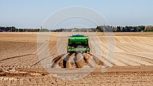 Farmland with a green tractor plowing the land for planting potatoes, preparing the land in a farm field