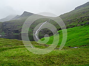 Faroe Islands. Green grass fields of Saksun. Waterfall in the background.
