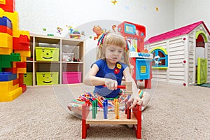 Fascinated little girl playing with wooden hammer in kindergarten