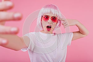 Fascinating young woman in peruke and funny sunglasses posing on pastel background. Indoor shot of