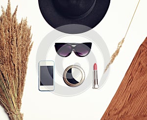 Fashion accessory, black hat, sunglasses, screen smartphone, pocket mirror and red lipstick on white background